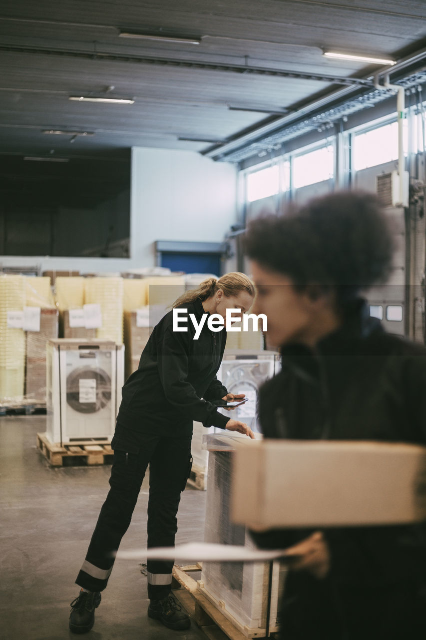 Businesswoman analyzing box containers with female manual worker at warehouse