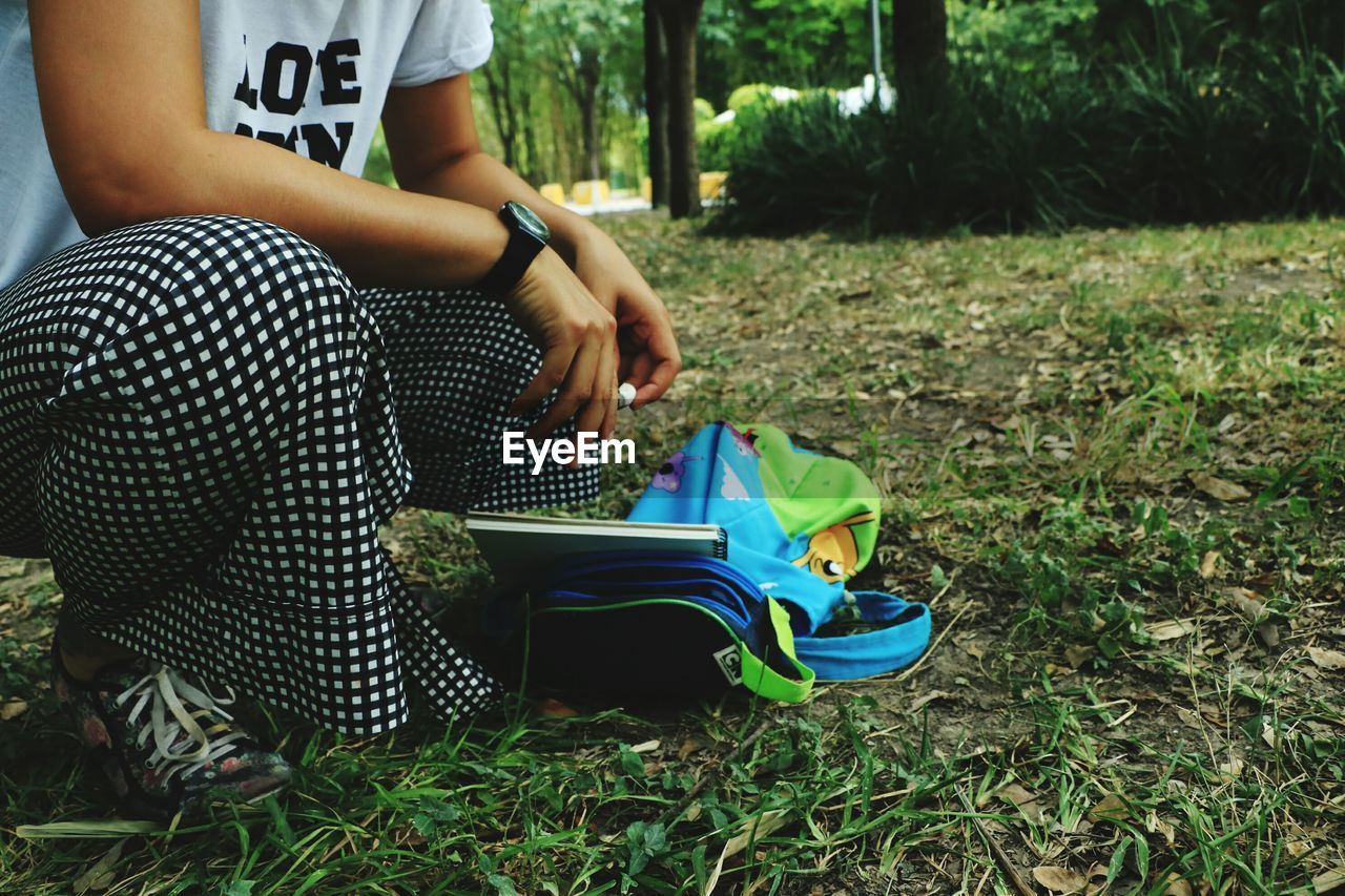 Low section of woman crouching by bag on field