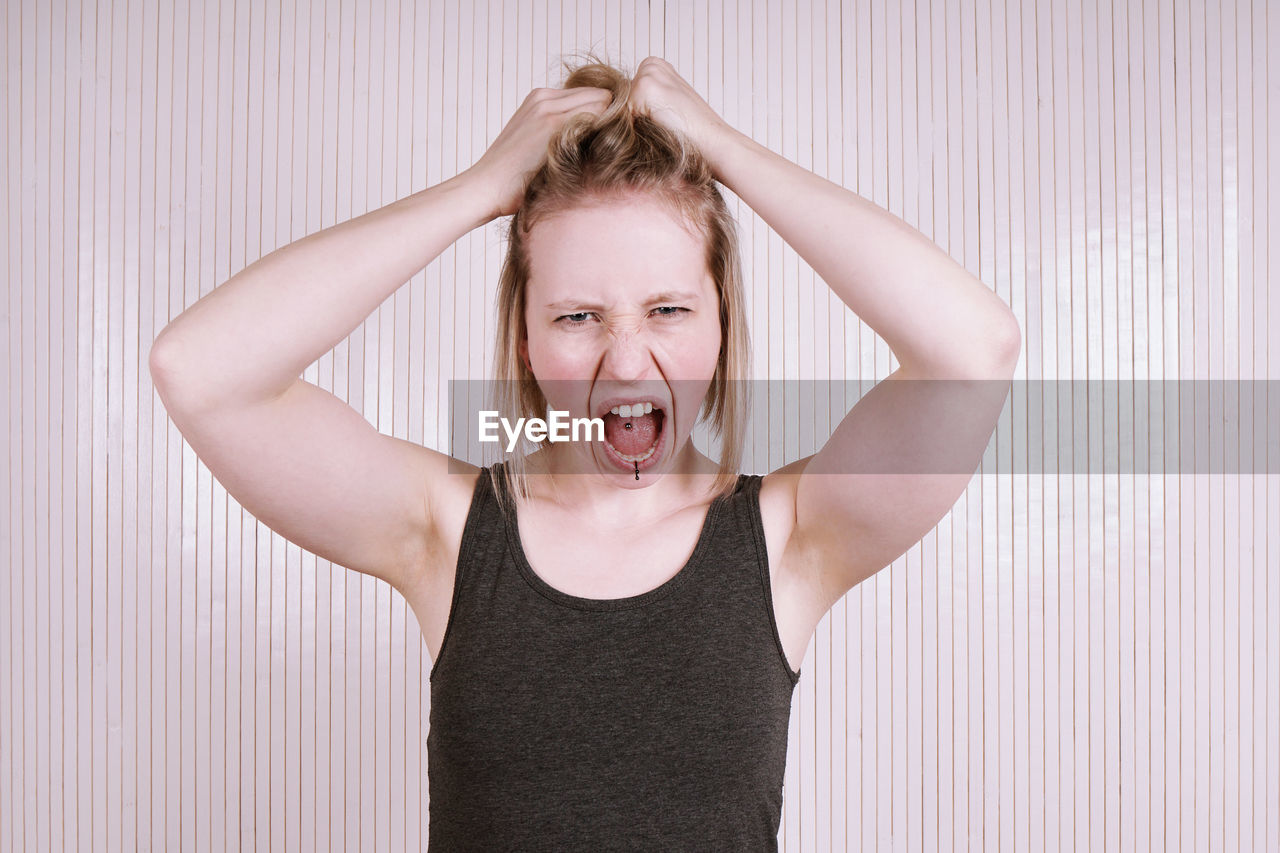 Portrait of young woman screaming against blinds