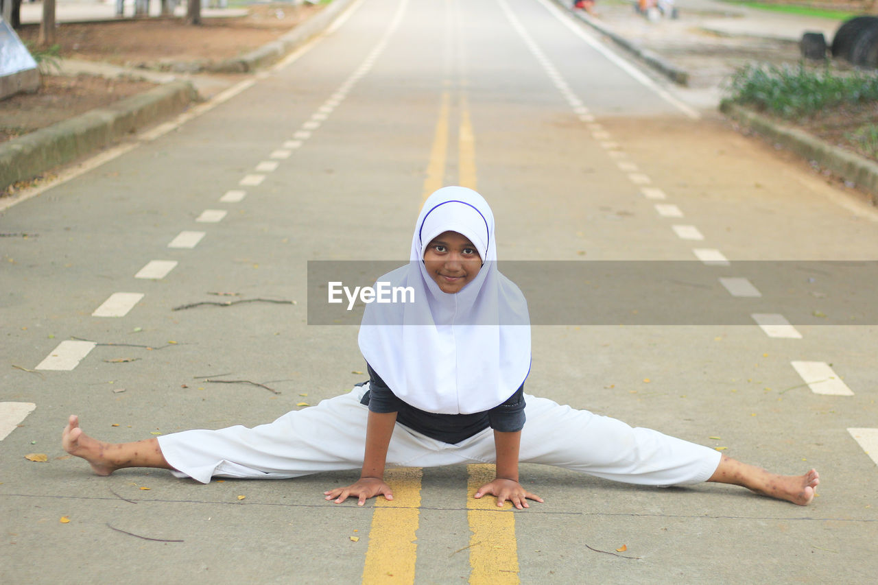 Portrait of girl in hijab doing splits on road