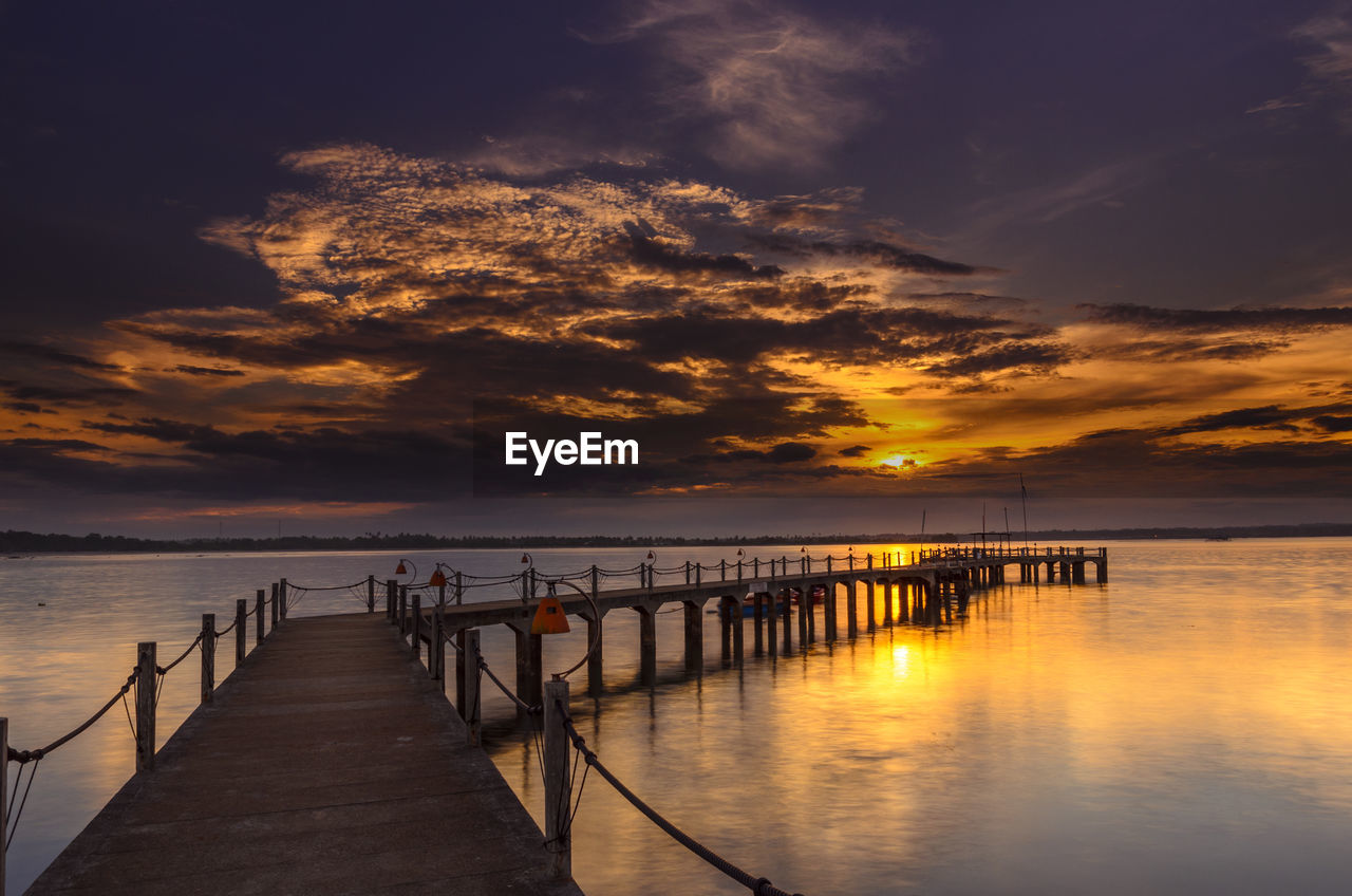 Silhouette pier over sea against cloudy sky during sunset