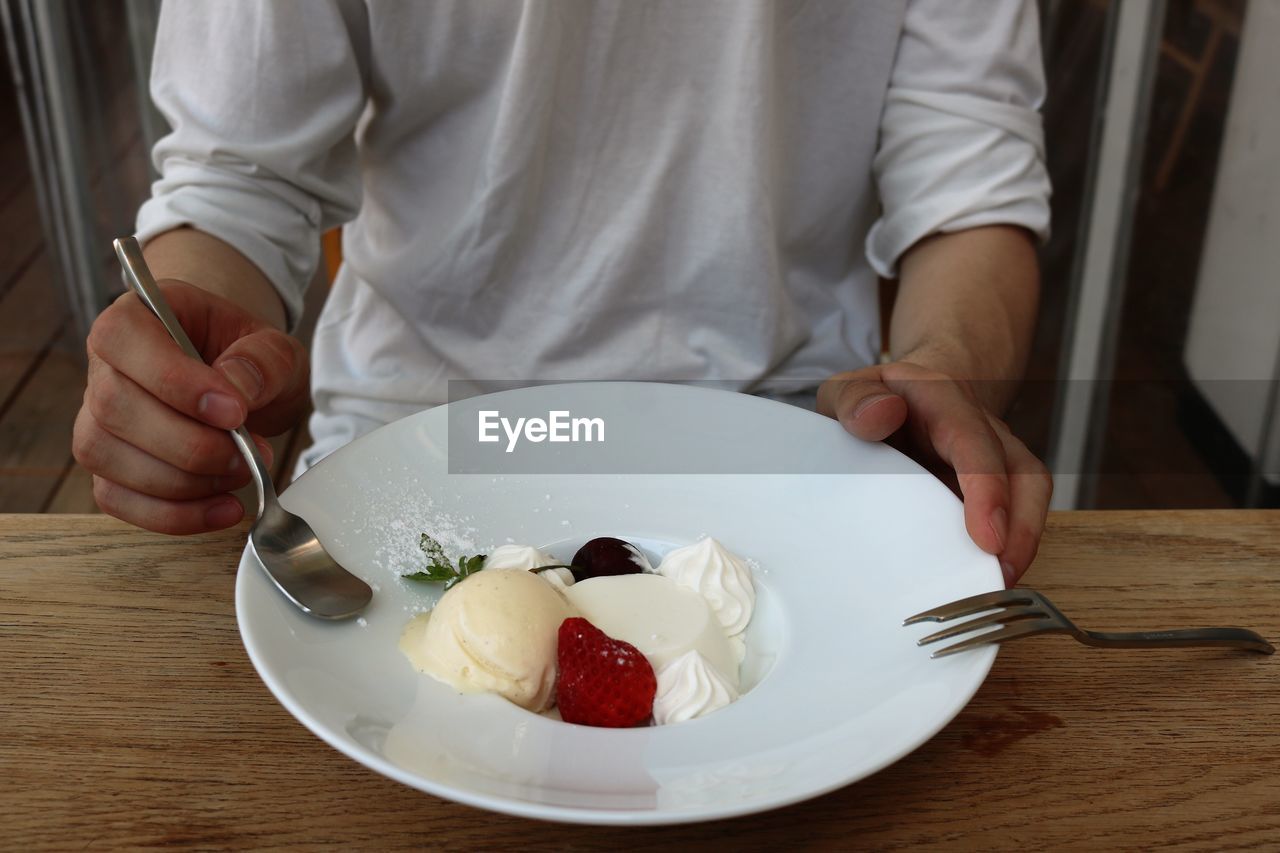 Midsection of man eating dessert at table