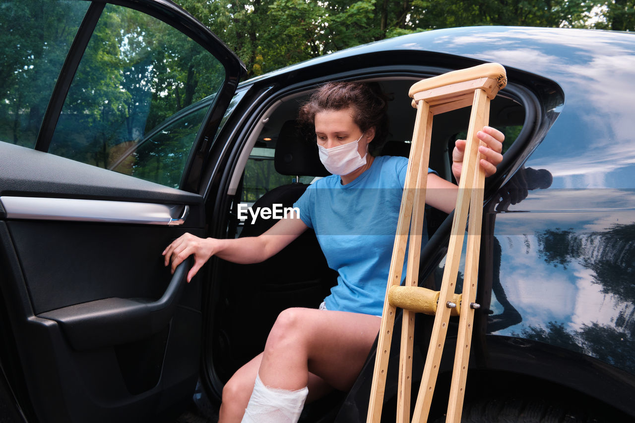 A woman with an injured leg gets into a car. orthopedic plaster, orthopedic crutches. 