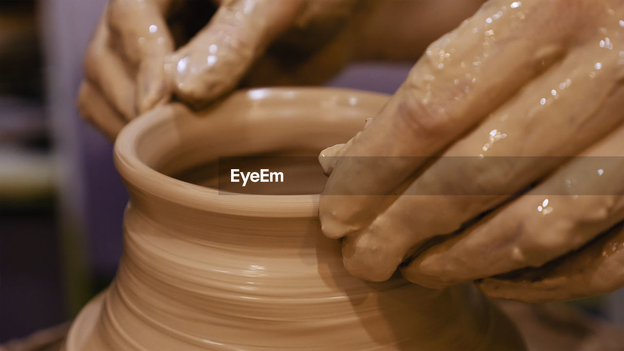 Cropped hands of craftsperson making clay product in pottery workshop