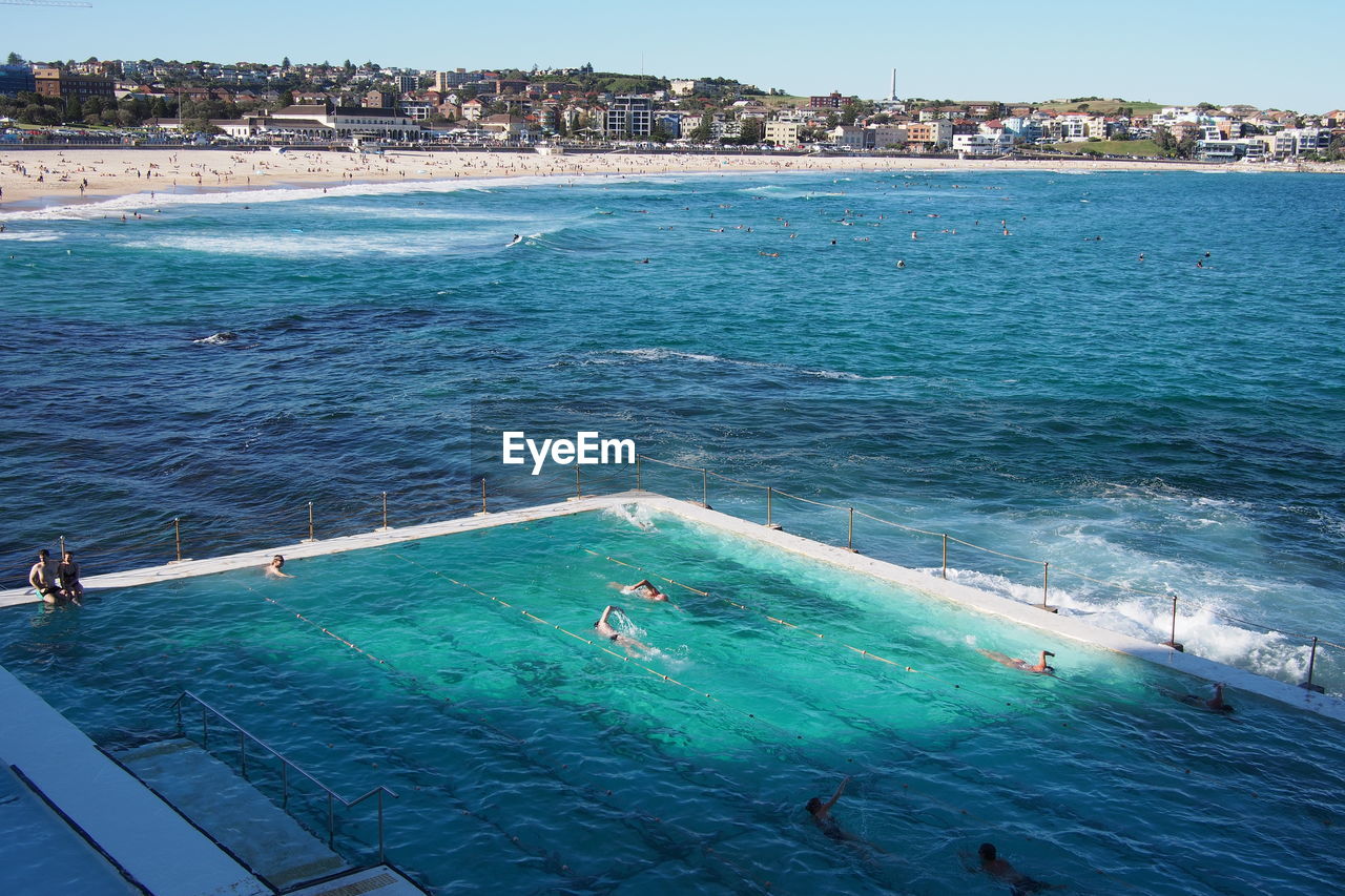 High angle view of people in swimming pool by sea against sky