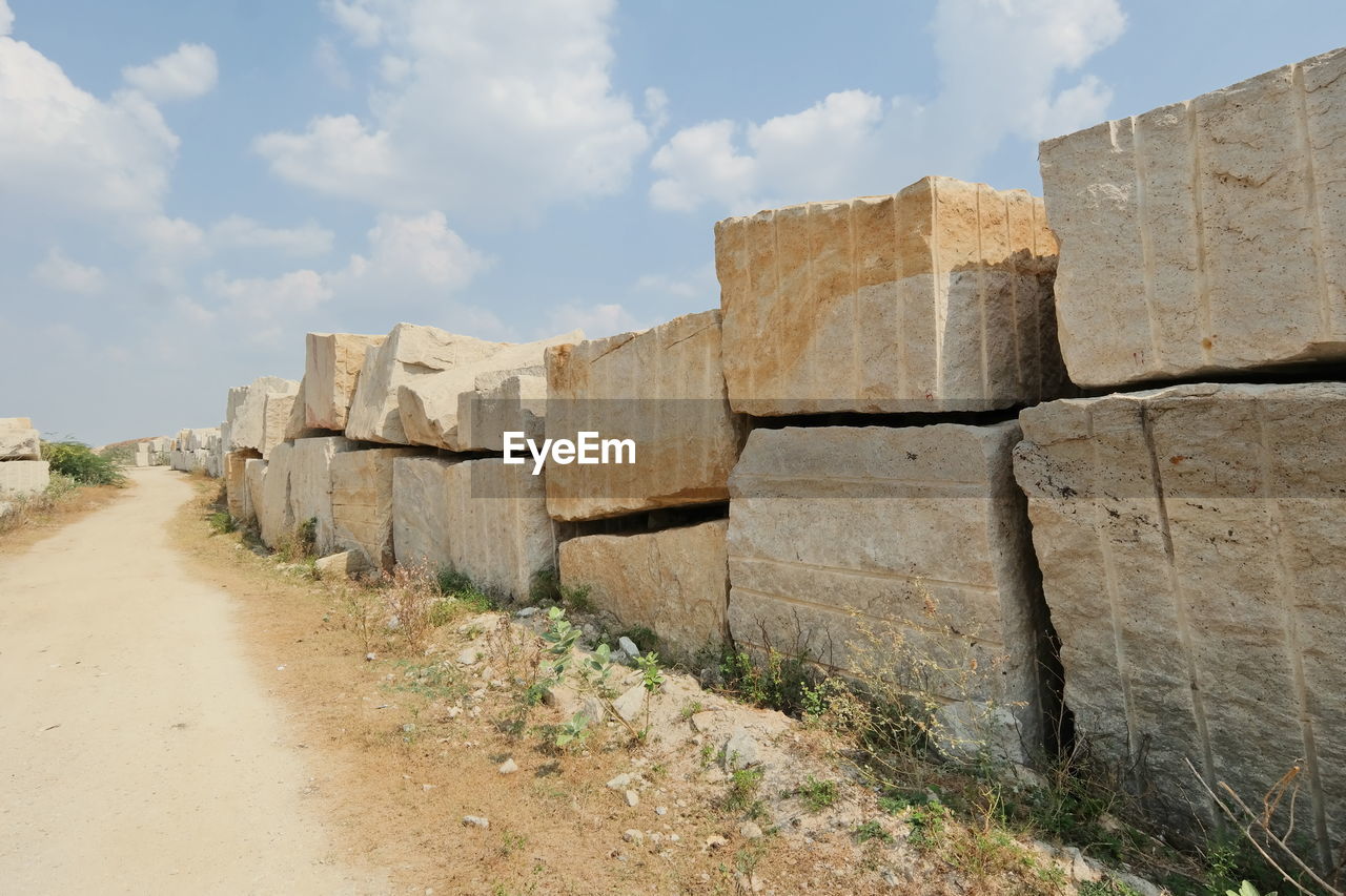 Dirt road by stone blocks against cloudy sky