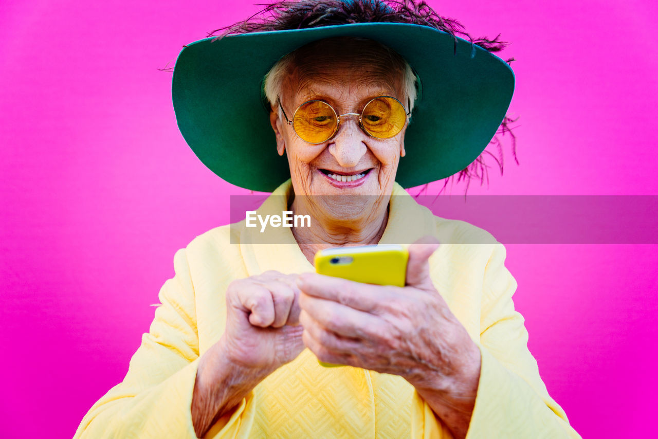 Close-up of smiling senior woman using phone against pink background