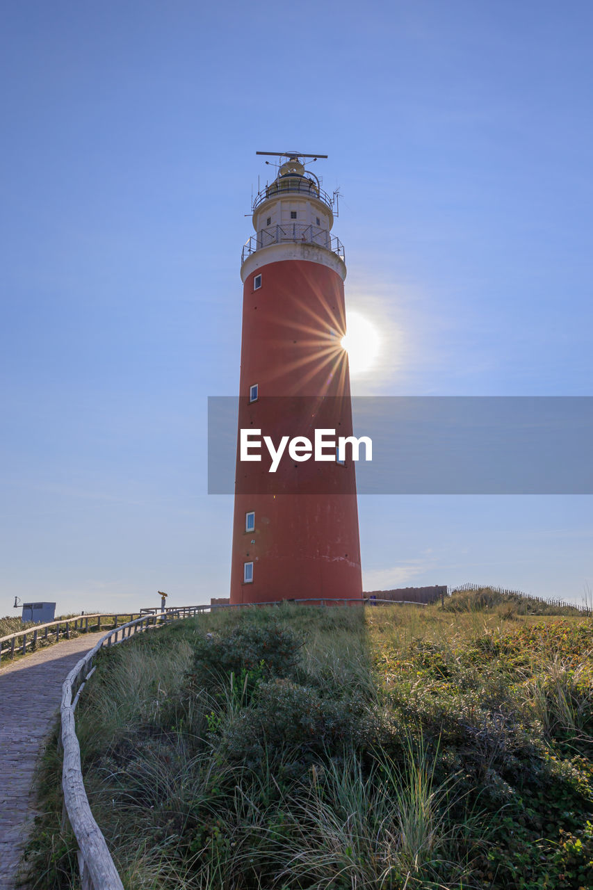 Lighthouse by sea against sky with sunstar