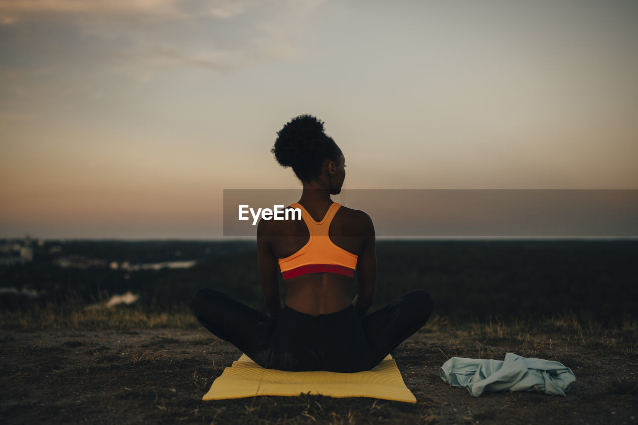 Rear view of sportswoman sitting on exercise mat during sunset