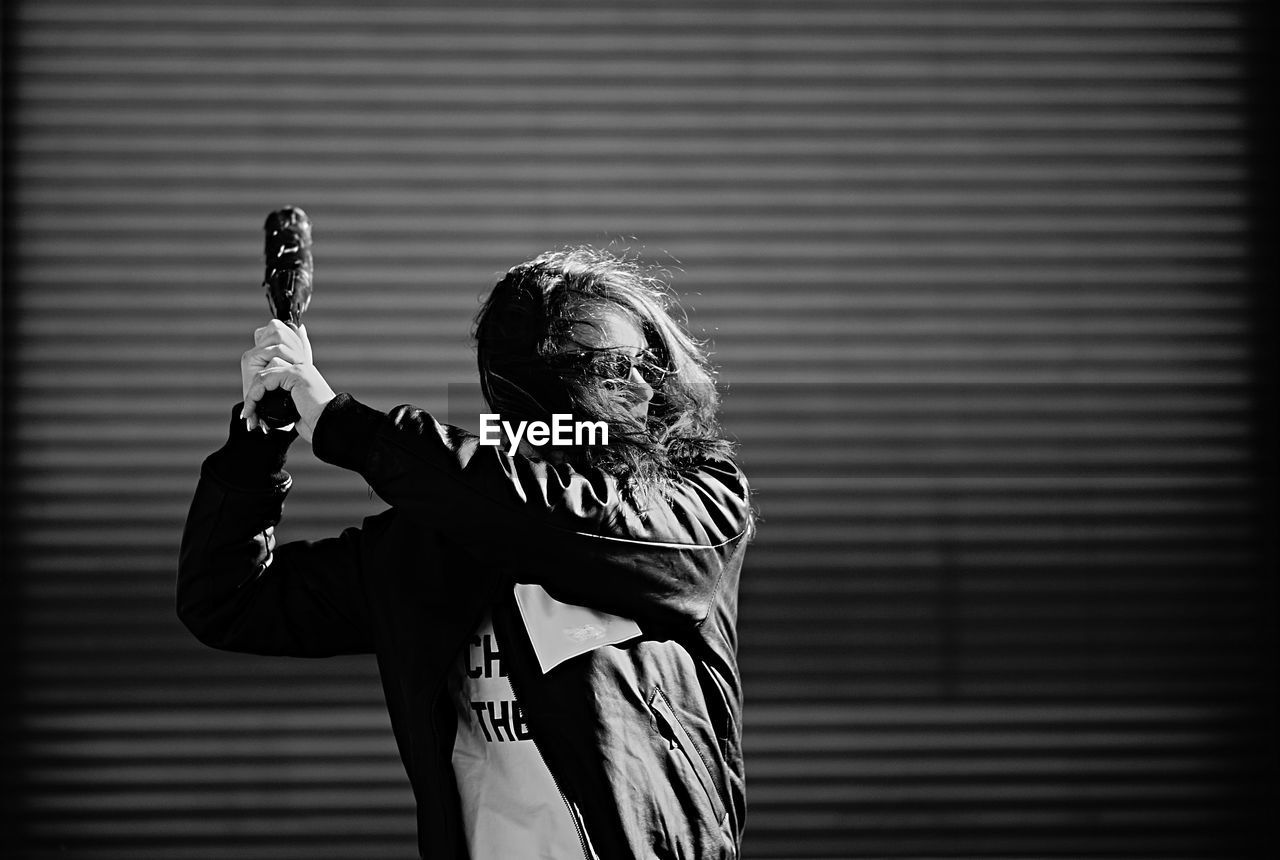 Woman holding baseball bat while standing against shutter