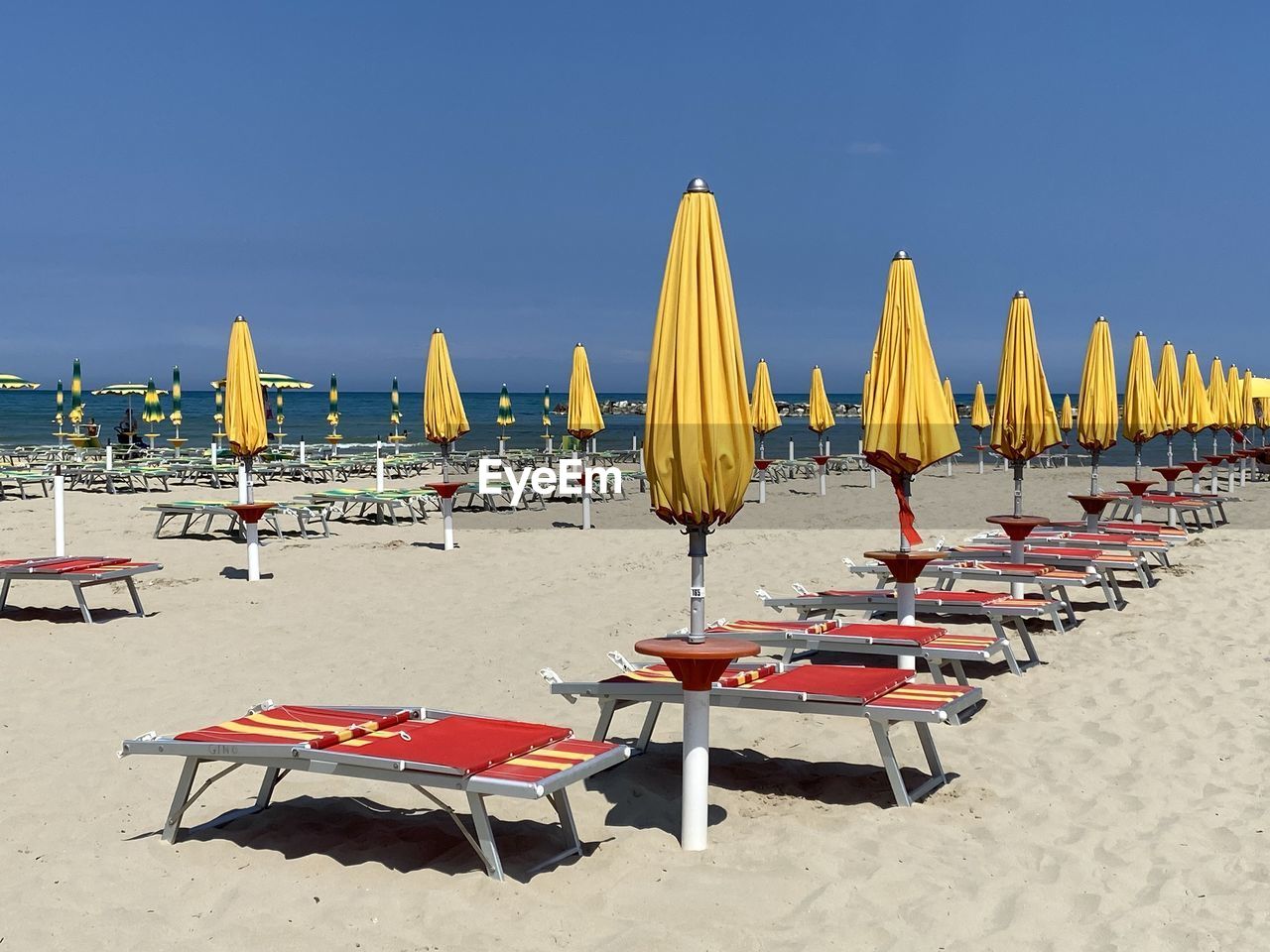 beach, land, sand, chair, sky, sea, nature, water, parasol, summer, seat, umbrella, lounge chair, beach umbrella, in a row, vacation, holiday, deck chair, trip, travel destinations, clear sky, sunshade, sunlight, relaxation, sunny, shade, beauty in nature, scenics - nature, outdoor chair, no people, tranquility, travel, day, outdoors, horizon, blue, absence, large group of objects, tranquil scene, horizon over water, copy space, idyllic, architecture, table, group of objects, tourism, arrangement, furniture