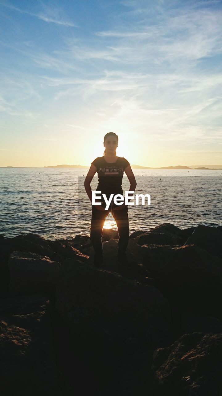 Woman performing yoga on sea shore against sky at morning