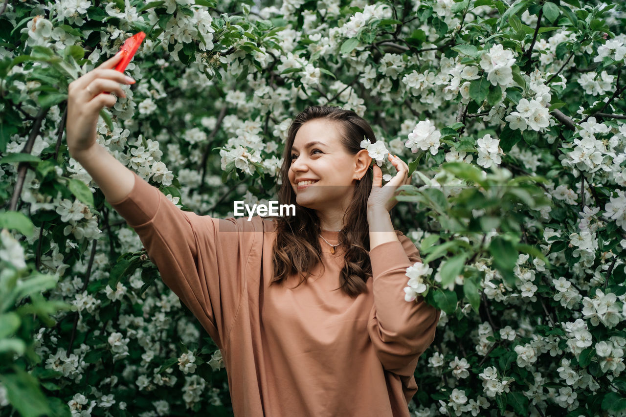 Girl in blooming apple tree using smartphone video call outdoor nature