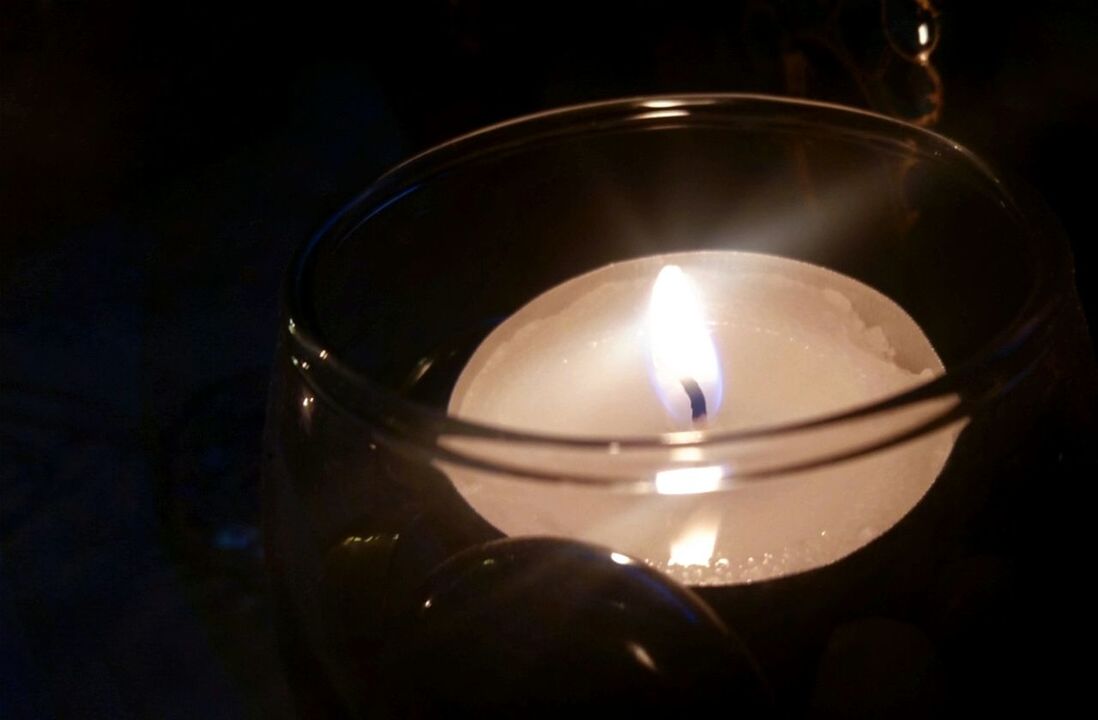 CLOSE-UP OF LIT TEA LIGHT CANDLES IN DARK ROOM