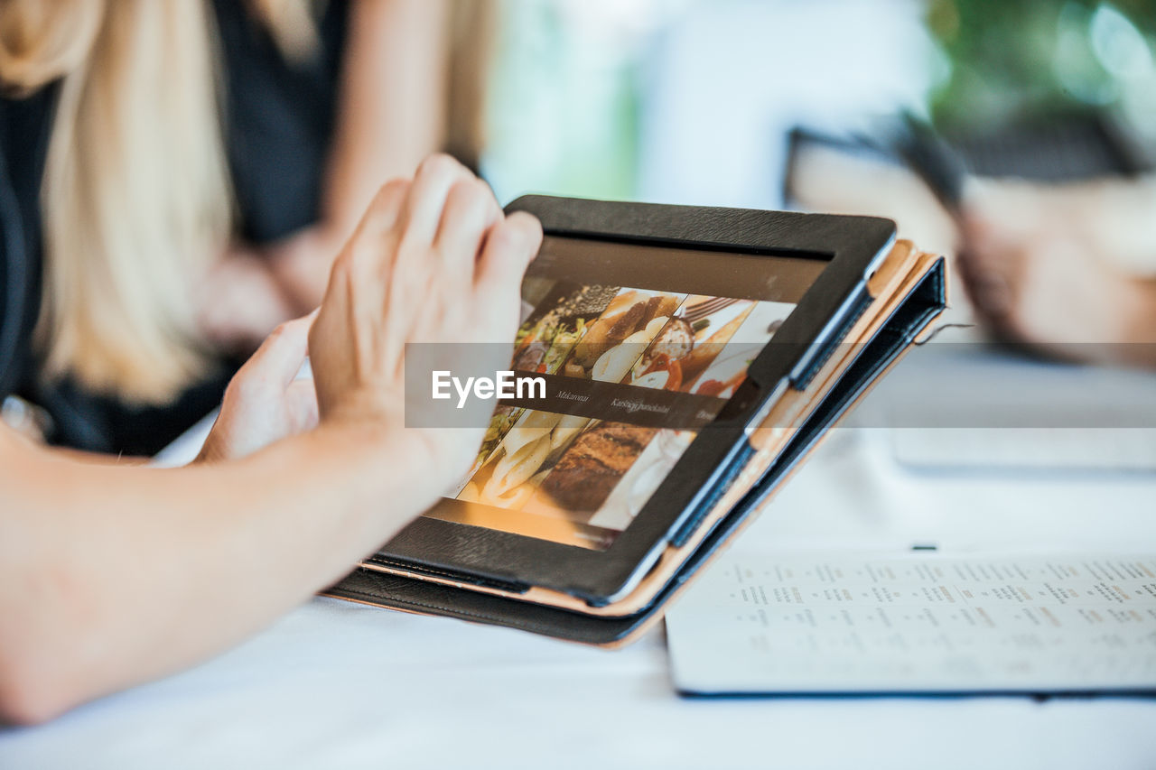 Cropped hand of woman using digital tablet on table