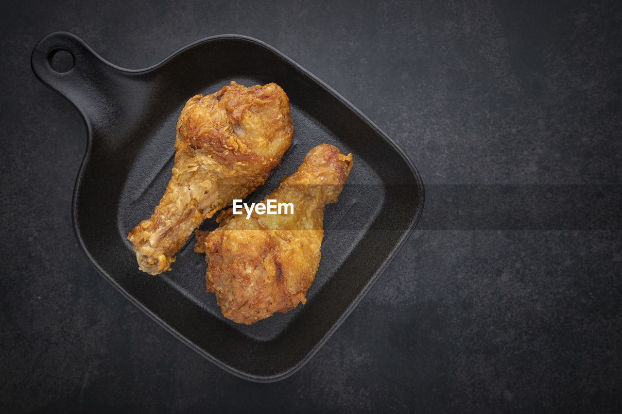 Crispy fried chicken drumstick in skillet pan on the dark tone background with copy space for text