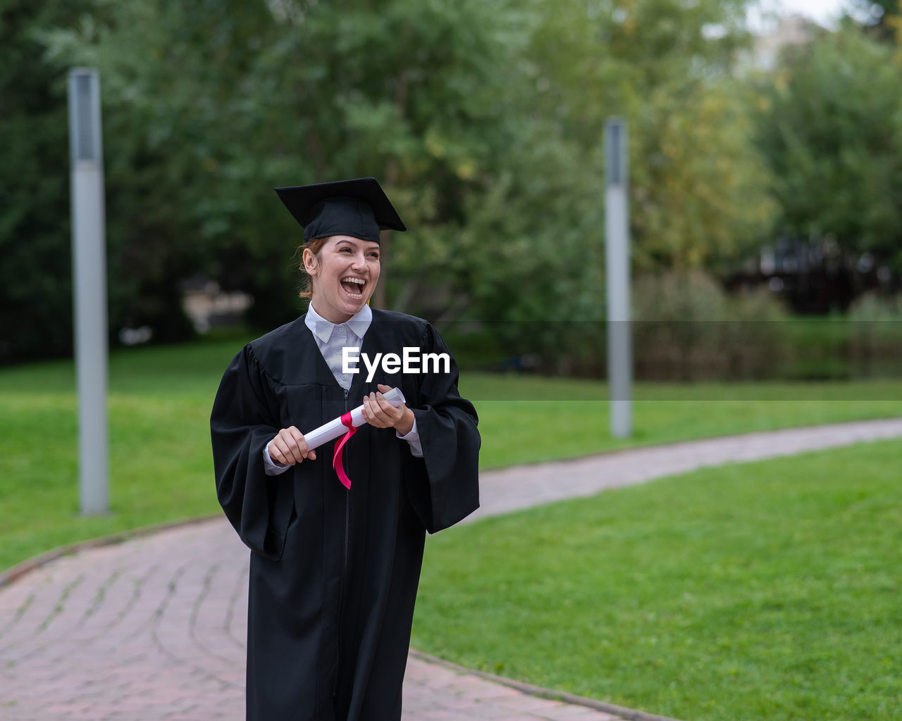 portrait of young woman wearing graduation gown standing against trees