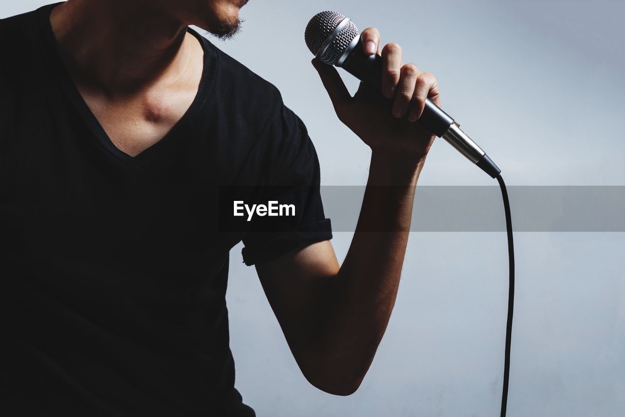 Midsection of man holding microphone while singing against gray background