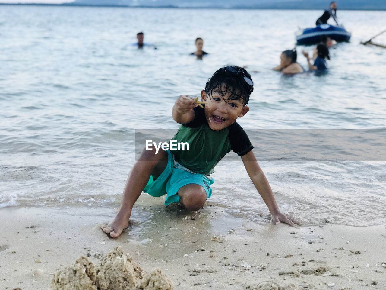 Portrait of cheerful boy crouching while holding starfish at seashore
