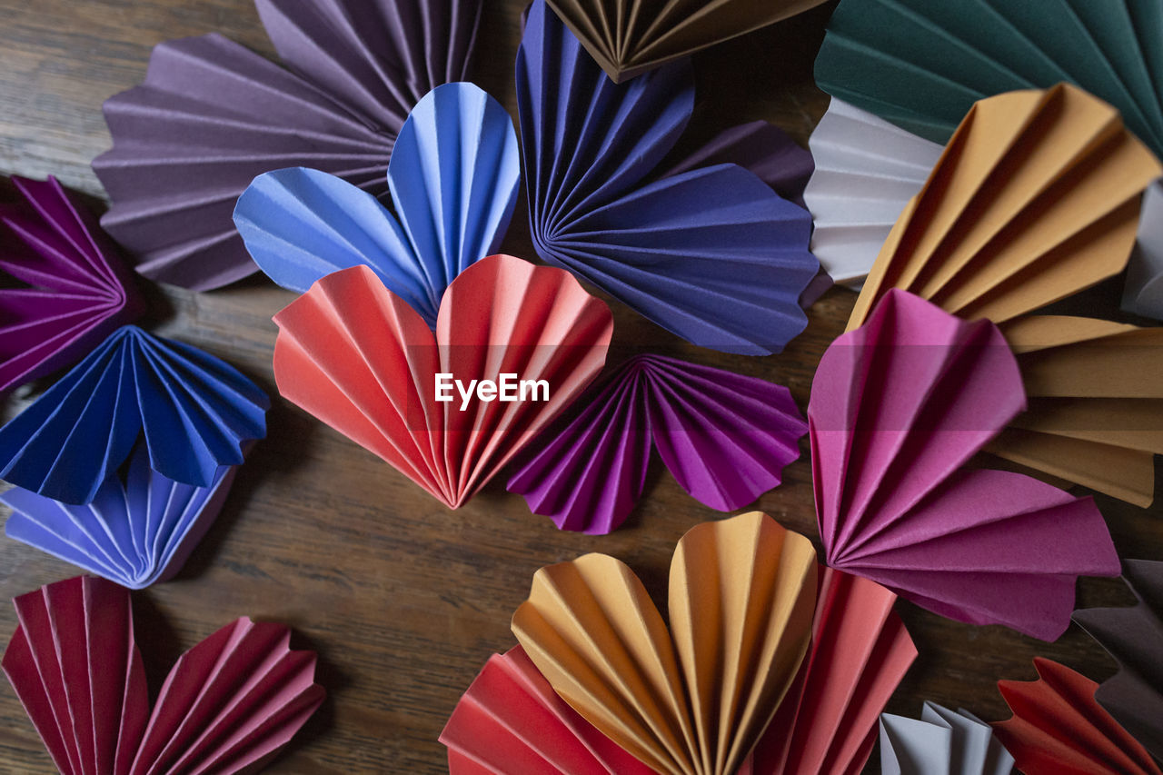 Multi-colored paper origami hearts arranged on wooden background