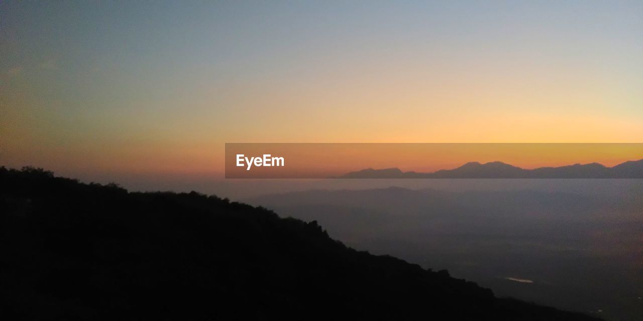 SCENIC VIEW OF SILHOUETTE MOUNTAINS AGAINST ORANGE SKY