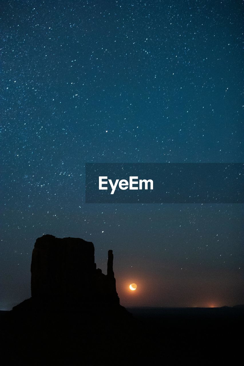 A crescent moon rises over the valley floor in monument valley