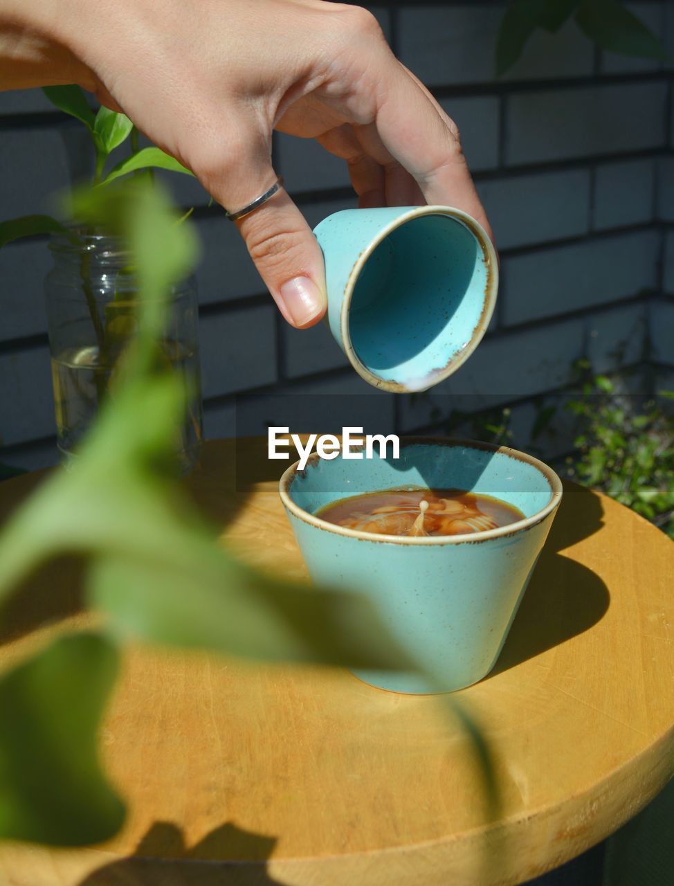 CROPPED IMAGE OF PERSON POURING COFFEE CUP