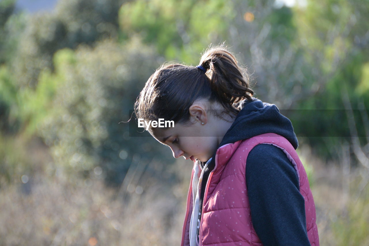 Side view of girl looking down against trees