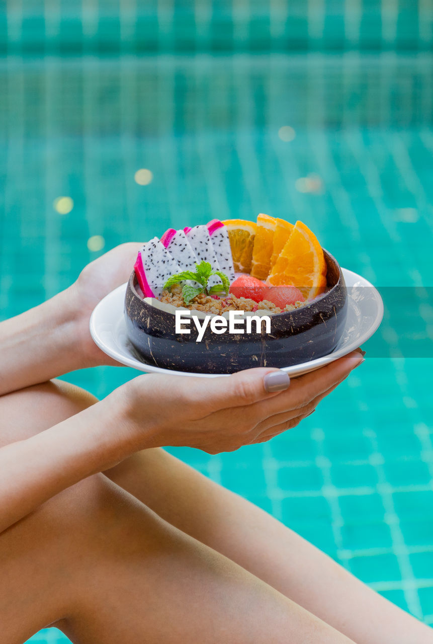 Woman holding smoothie bowl with fresh fruits by swimming pool