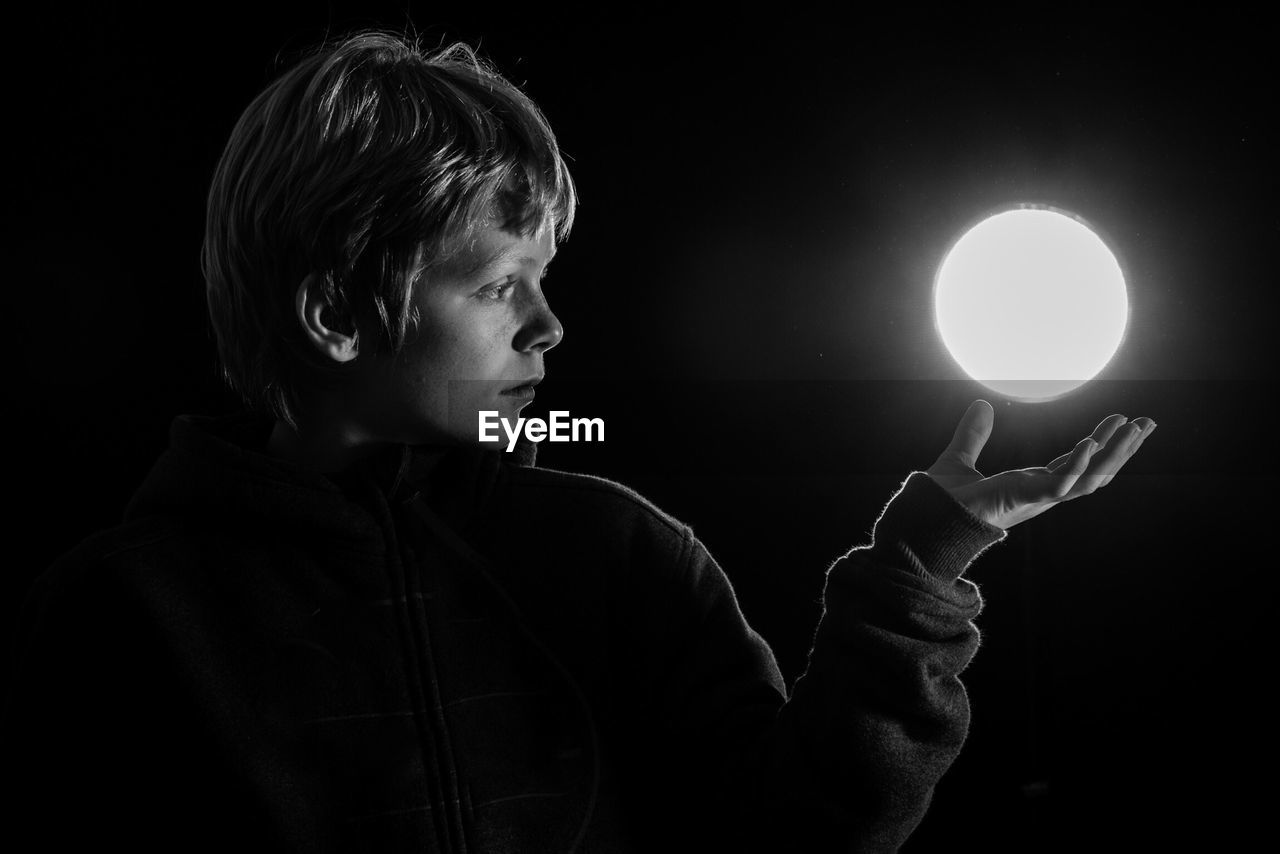 Optical illusion of boy levitating illuminated glowing sphere against black background