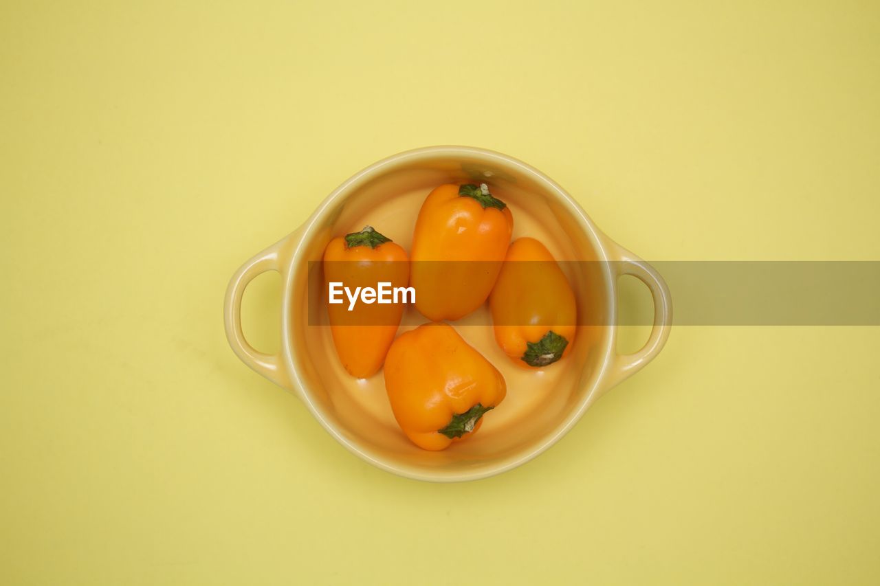 Directly above view of orange peppers in bowl against yellow background
