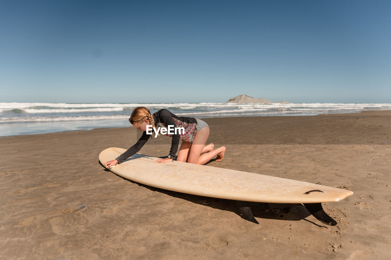 Young female waxing surfboard at a beach in new zealand