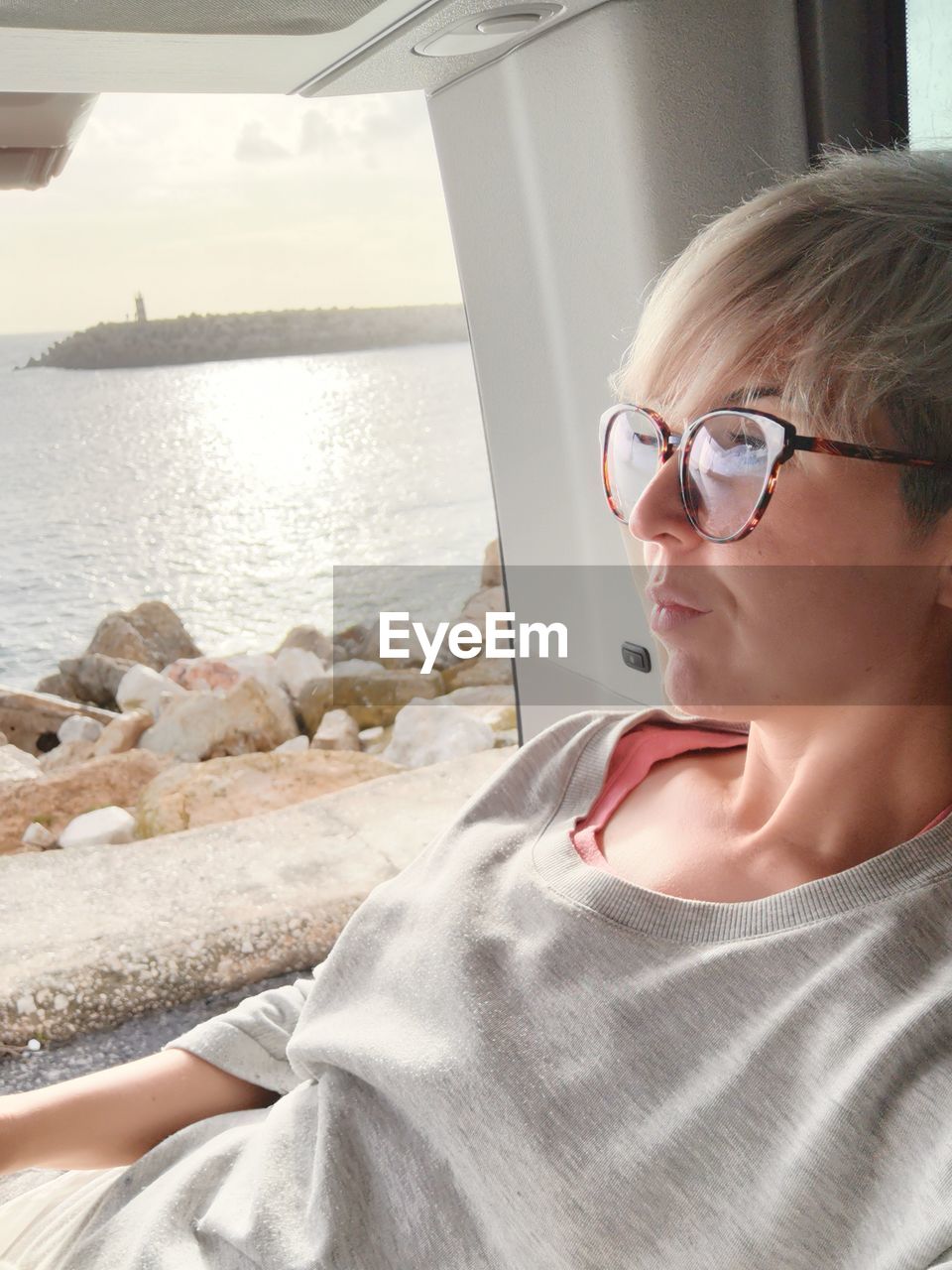 Woman looking away while relaxing by motor home window at beach