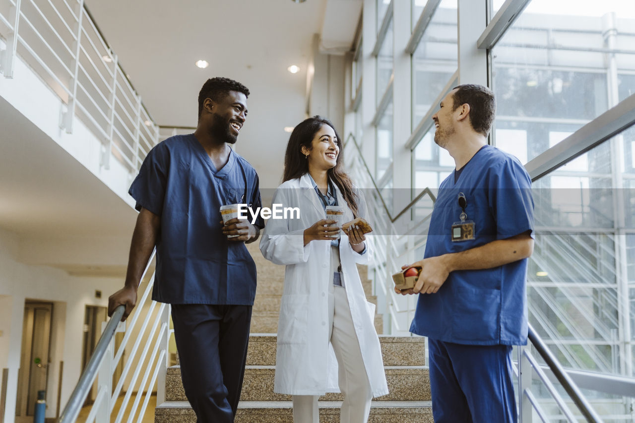 Happy multiracial healthcare workers talking while standing on staircase at hospital