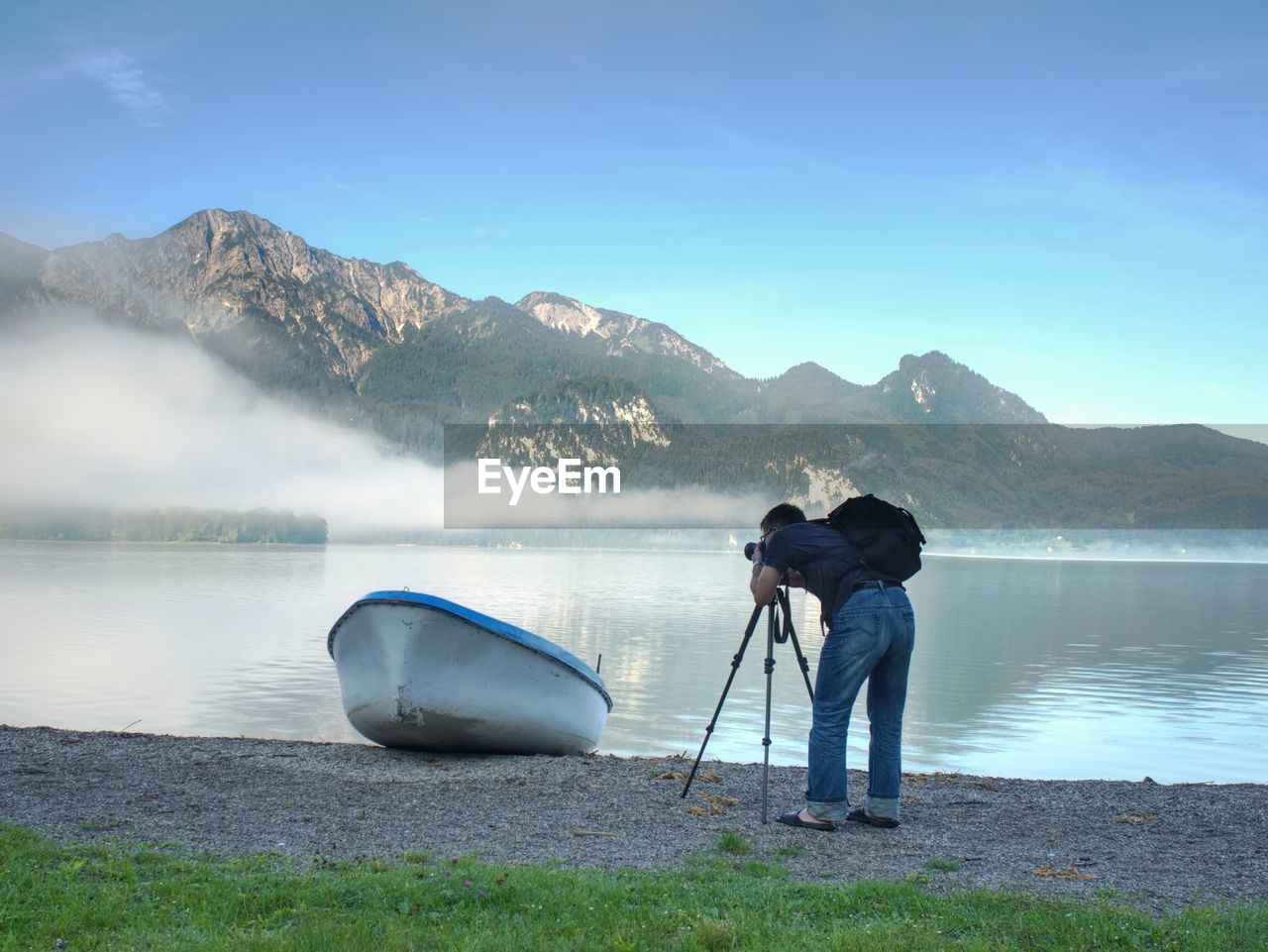 Man hiker is taking photo of ship at mountain lake shore. silhouette at fishing paddle boat at lake