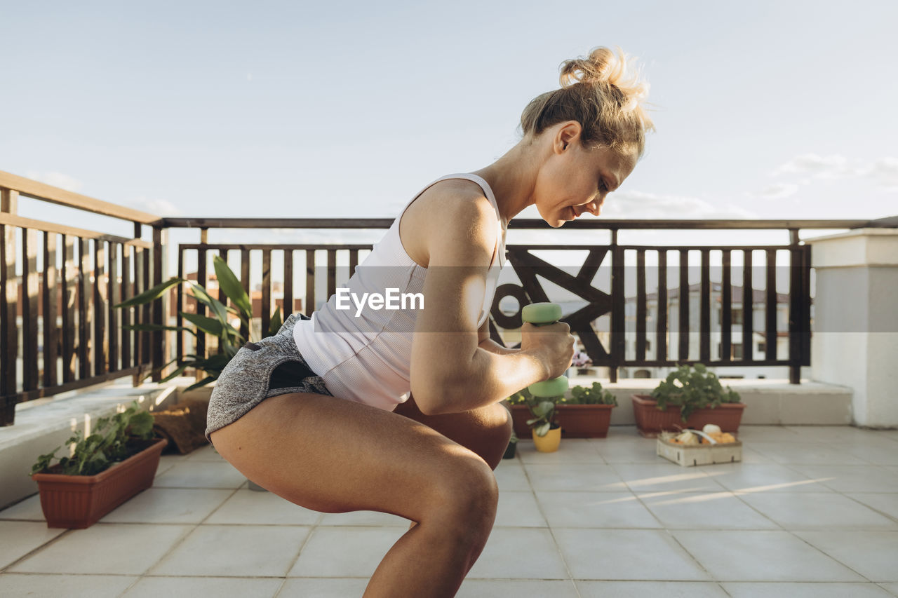 Woman doing exercises with dumbbells on roof terrace