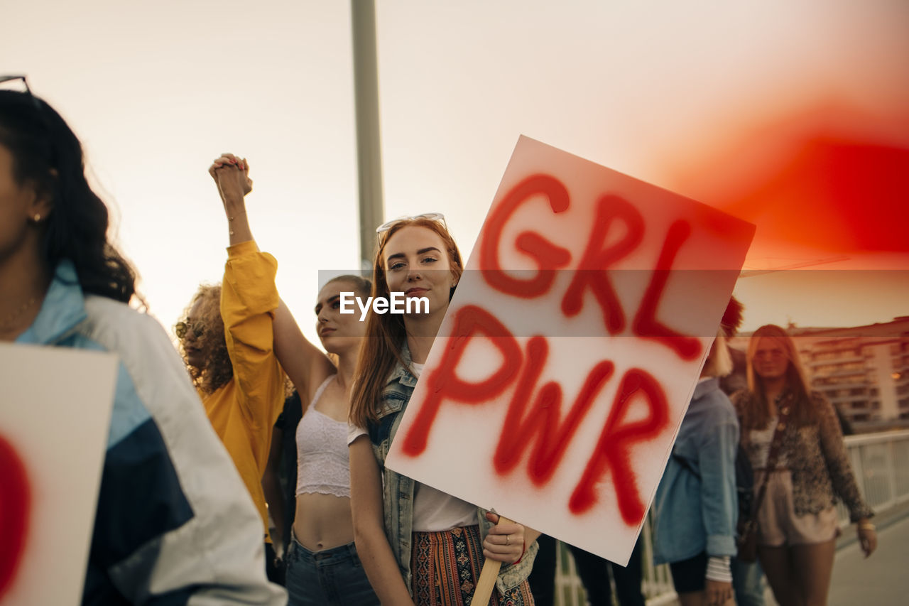 Portrait of women protesting with friends for human rights in city against sky