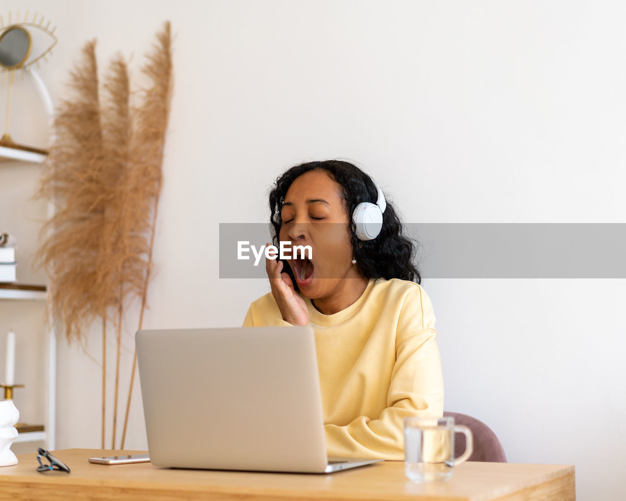 African-american female student yawning while listening to online lecture in headphones on laptop