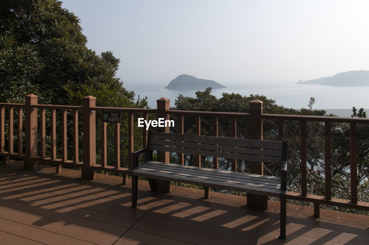 Empty bench by railing against sky