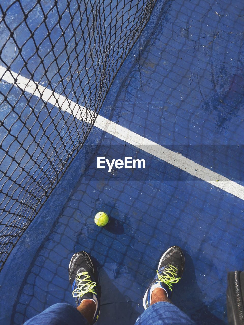 Low section of man standing by net and ball on blue tennis court