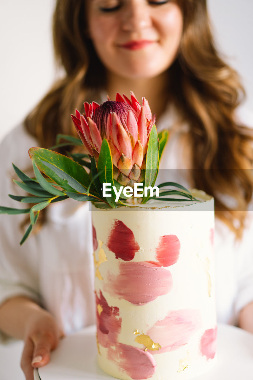 Young woman with birthday cake, close up. the cake is decorated with protea flowers.