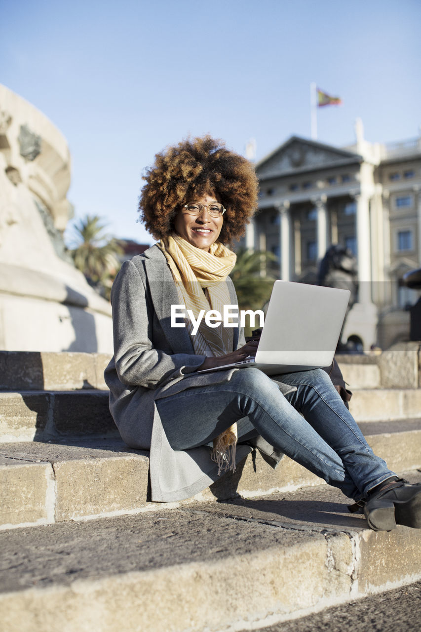 Portrait of smiling woman using laptop computer while sitting on steps