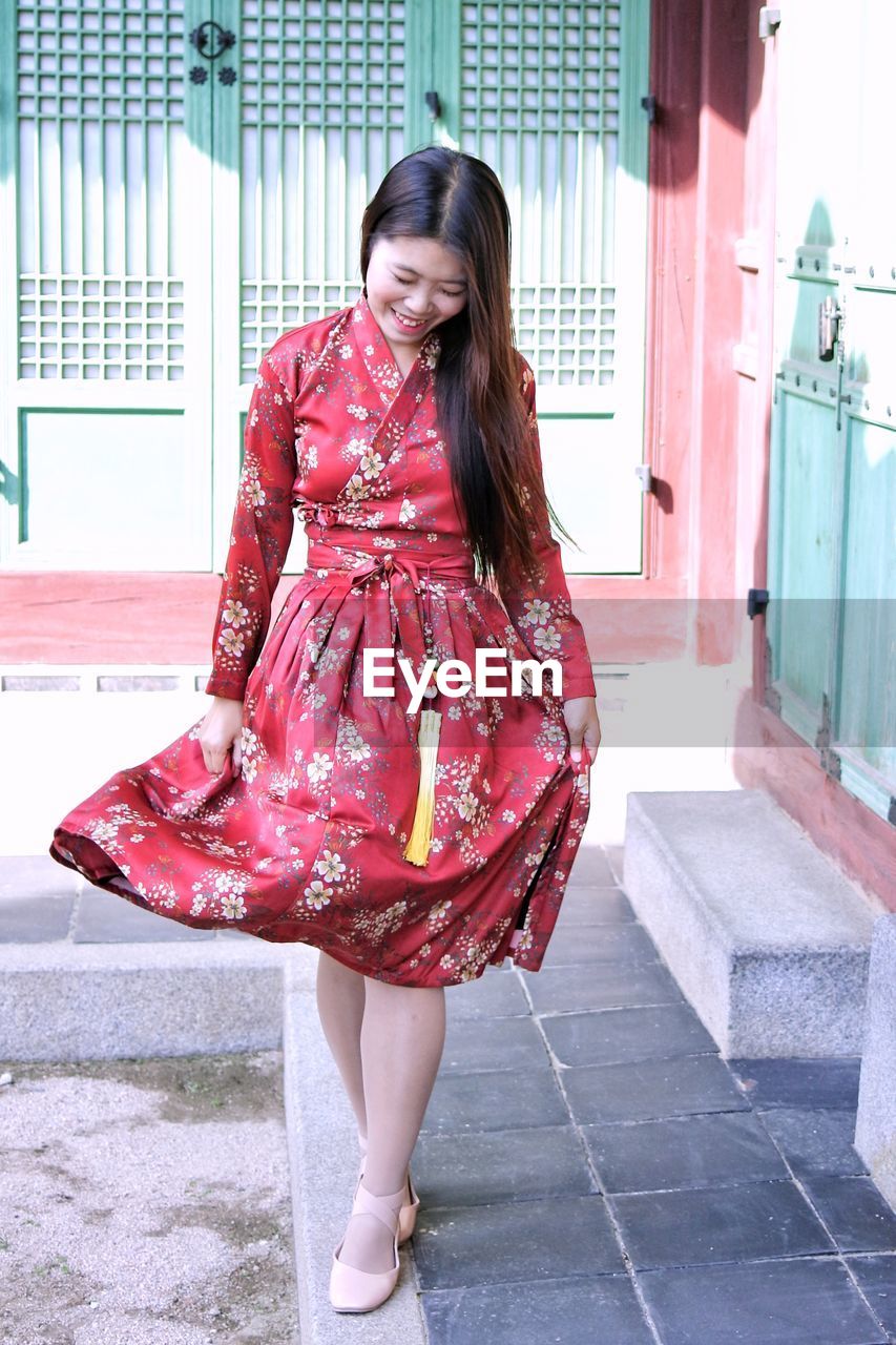 Full length of smiling young woman in floral dress walking outdoors