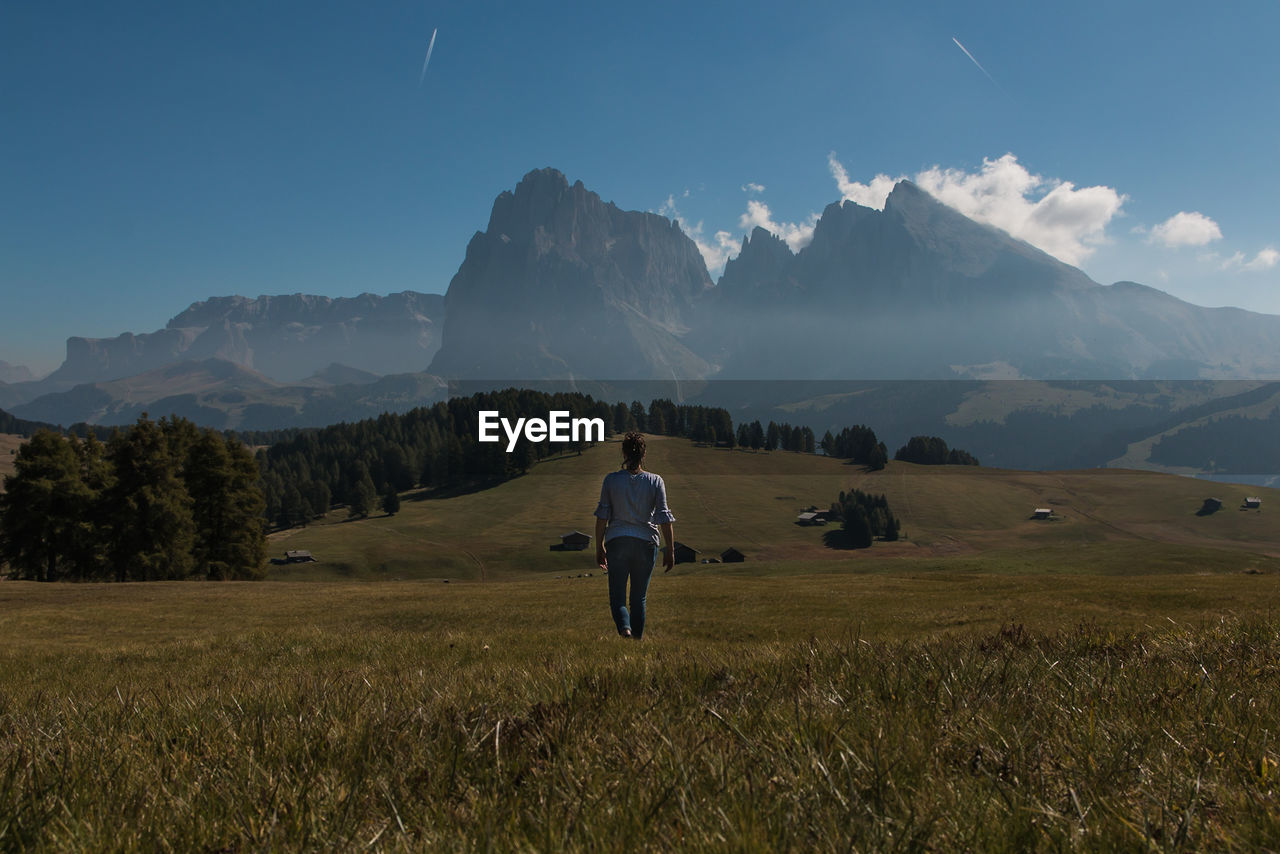 Rear view of woman walking on field towards mountains