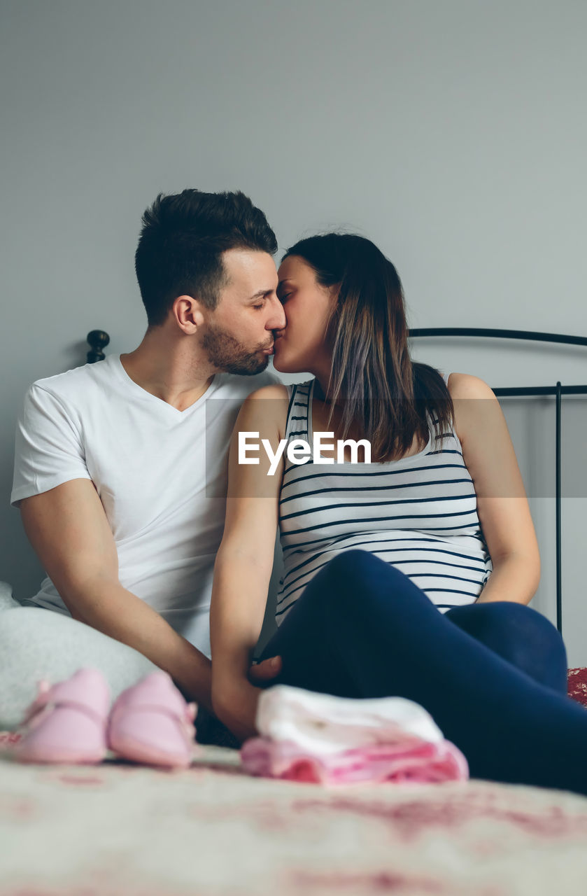 Couple kissing while sitting on bed at home