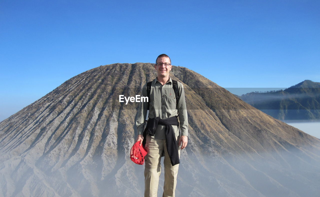 Portrait of man standing against mountain and clear blue sky