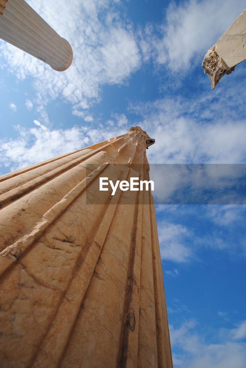 Low angle view of historic columns against cloudy sky