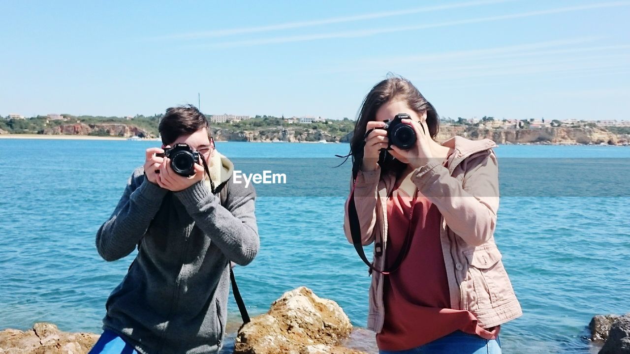 Friends photographing at sea shore against sky