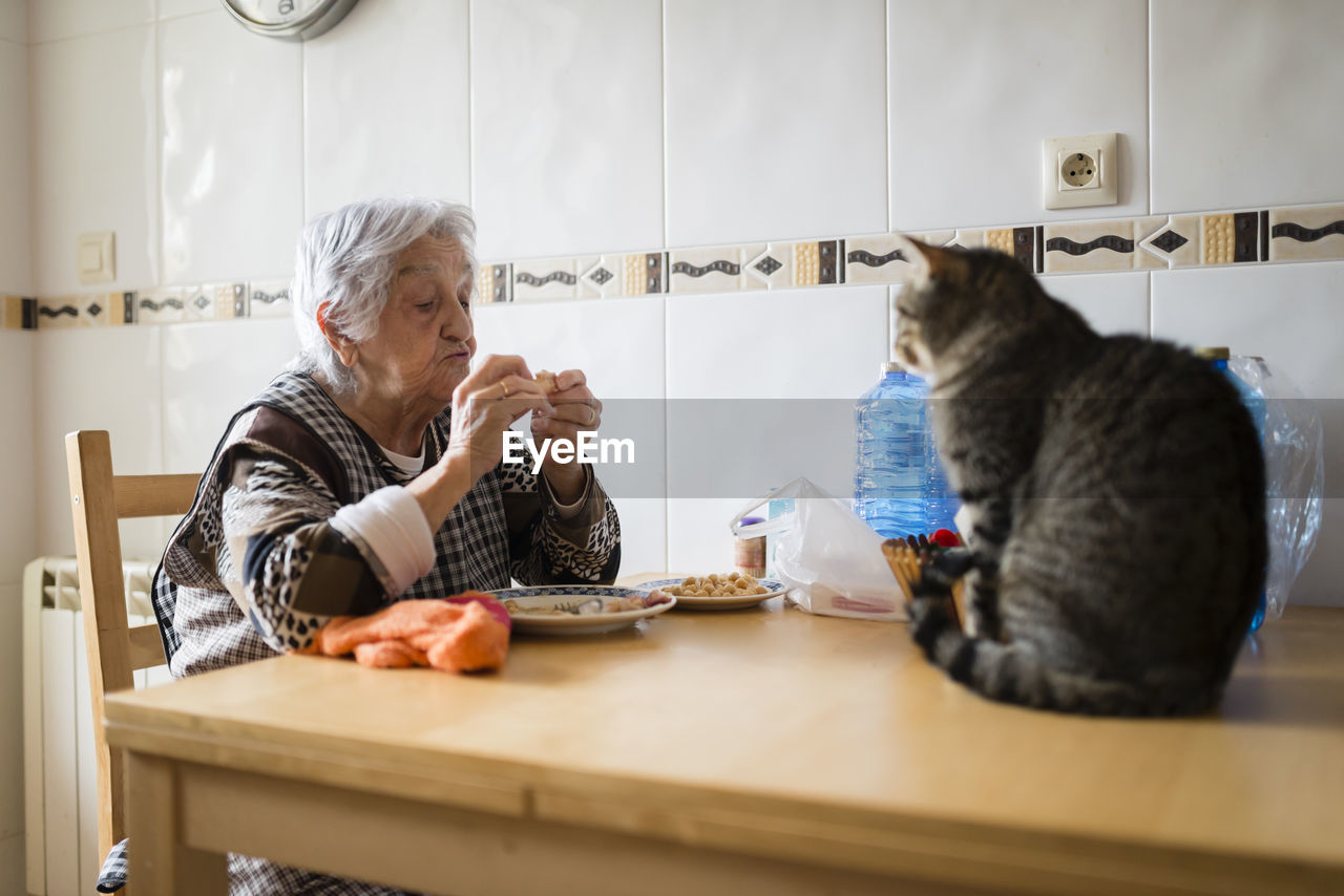 Senior woman eating while the cat watching her