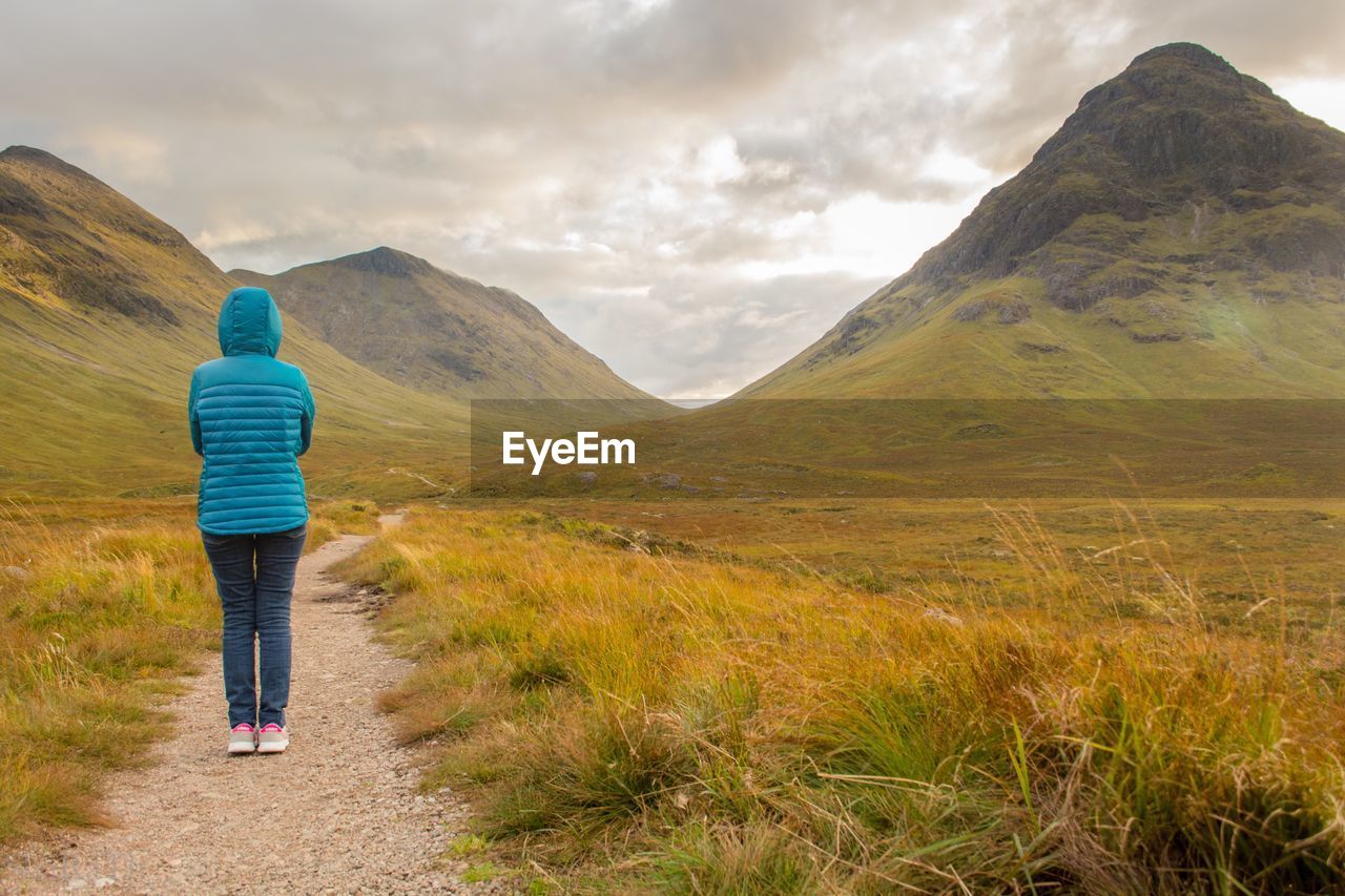 Rear view of woman standing on hiking trail against sky